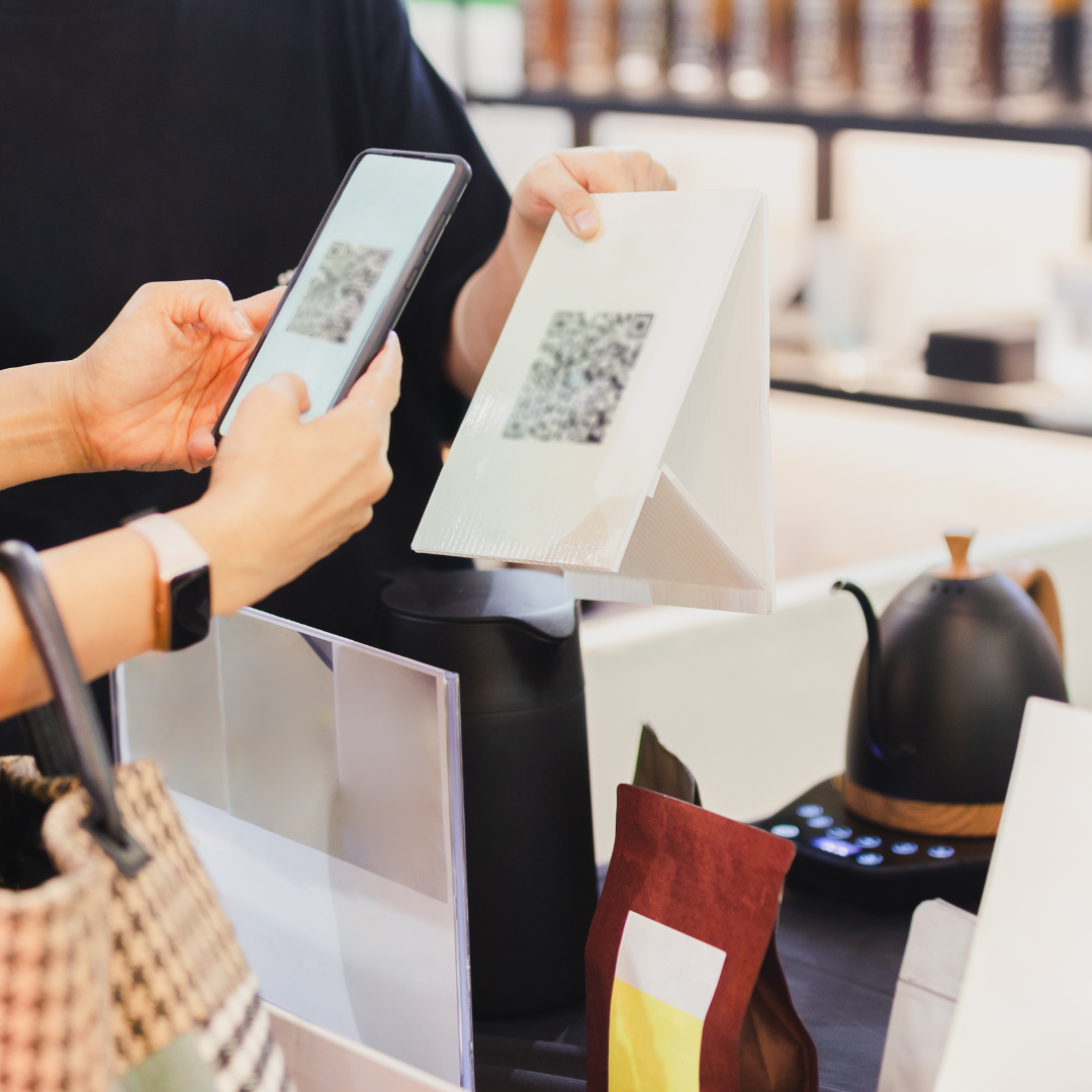 One person holds a piece of paper with a QR code printed on it, while another scans it with their smartphone.