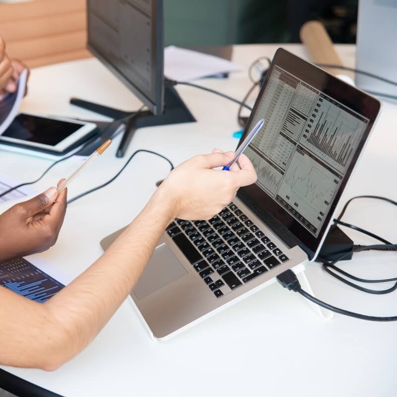 With a pen in hand, two people analyze the data from a computer screen.