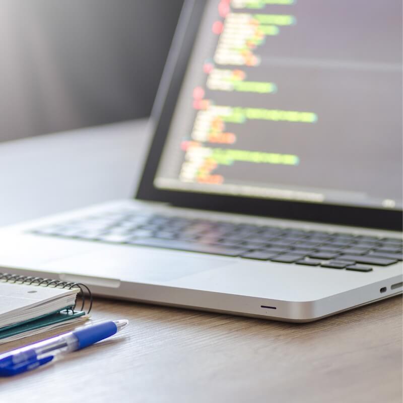 Pen and notebook lie in front of a computer, where code is being constructed on the screen.