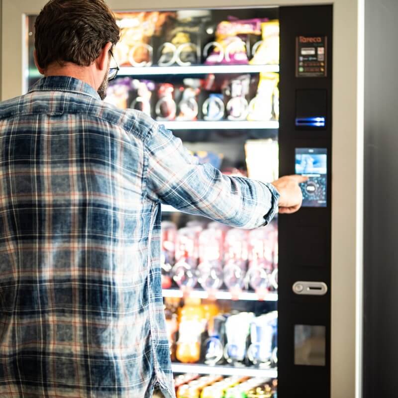 A man is seen selecting a product from a vending machine.